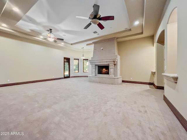 unfurnished living room with ceiling fan, light carpet, a large fireplace, recessed lighting, and a tray ceiling