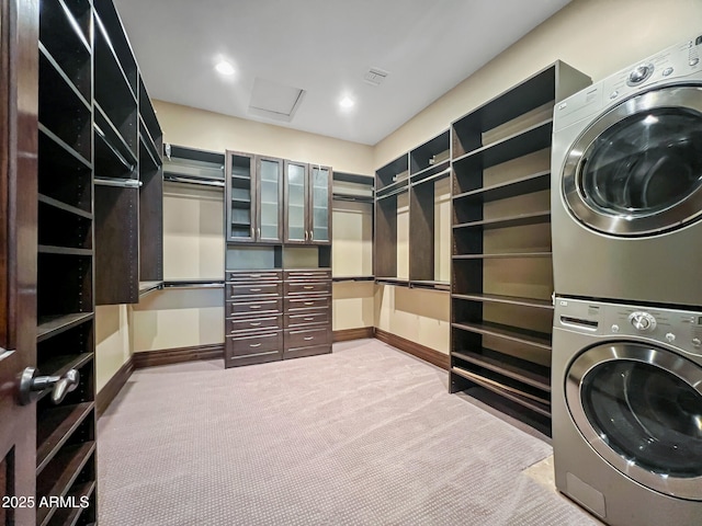 laundry room featuring laundry area, attic access, stacked washing maching and dryer, carpet floors, and baseboards