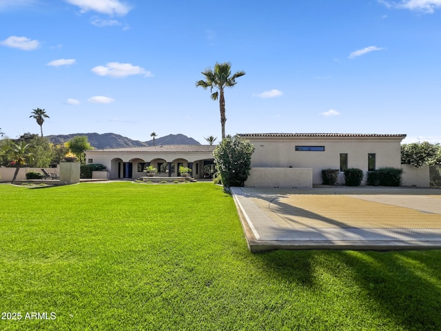 back of property with a mountain view, stucco siding, and a yard