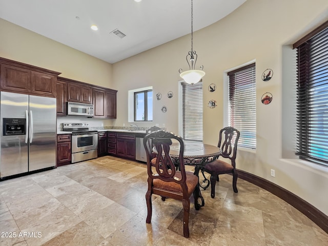kitchen featuring visible vents, stone tile flooring, a sink, decorative light fixtures, and stainless steel appliances