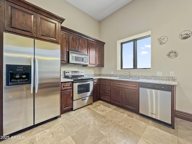 kitchen featuring stone finish floor, dark brown cabinets, a sink, light stone counters, and stainless steel appliances