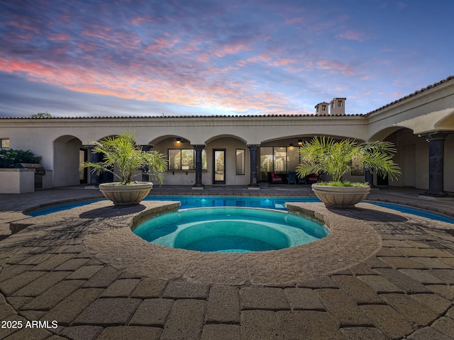 pool at dusk featuring a patio, a pool with connected hot tub, and a grill