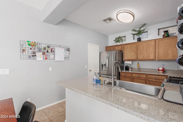 kitchen with light stone countertops, sink, kitchen peninsula, stainless steel refrigerator with ice dispenser, and light tile patterned floors