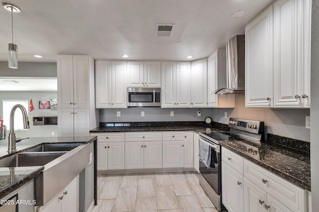 kitchen featuring pendant lighting, wall chimney range hood, sink, white cabinetry, and stainless steel appliances