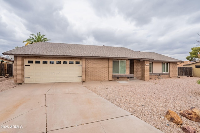 ranch-style home featuring concrete driveway, fence, brick siding, and roof with shingles