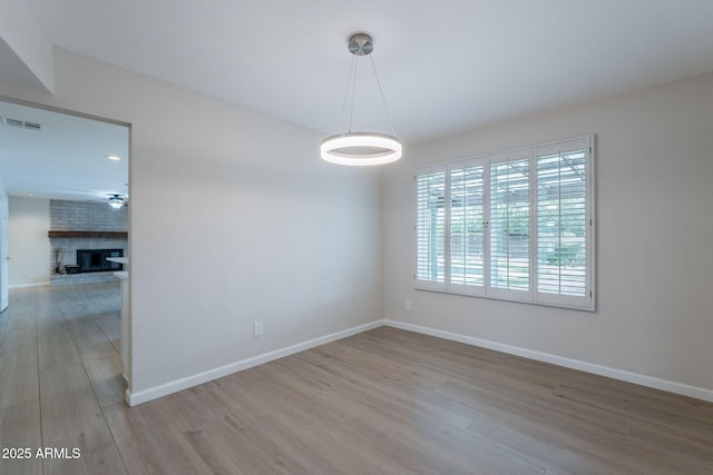 unfurnished room featuring wood finished floors, baseboards, and a brick fireplace