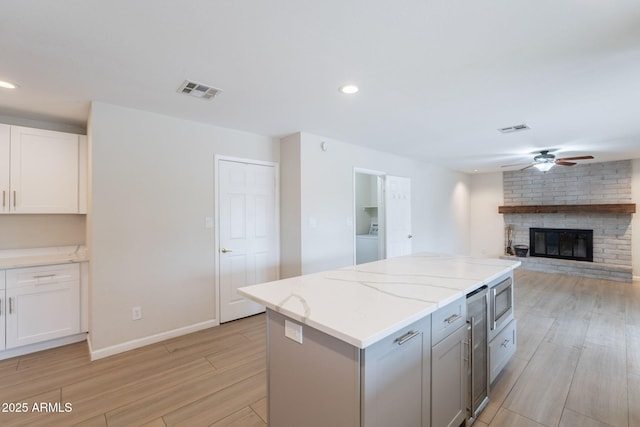 kitchen featuring a ceiling fan, washer / dryer, light wood finished floors, a brick fireplace, and white cabinetry