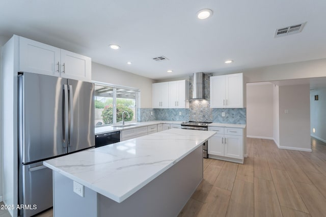 kitchen featuring appliances with stainless steel finishes, wall chimney range hood, a sink, tasteful backsplash, and white cabinets