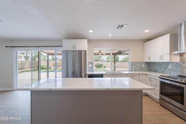 kitchen with stainless steel appliances, a sink, light wood finished floors, a kitchen island, and light stone countertops