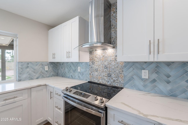 kitchen with stainless steel electric range, wall chimney range hood, white cabinets, light stone counters, and tasteful backsplash