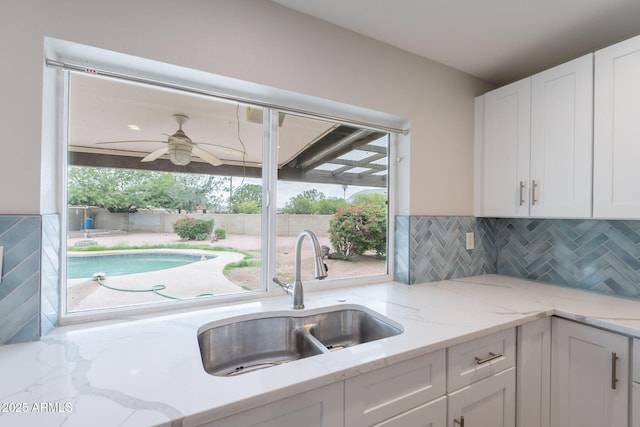kitchen with a sink, white cabinets, ceiling fan, and light stone countertops