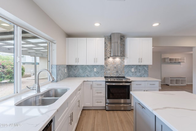 kitchen featuring wall chimney exhaust hood, stainless steel electric range oven, a sink, light wood-style floors, and tasteful backsplash
