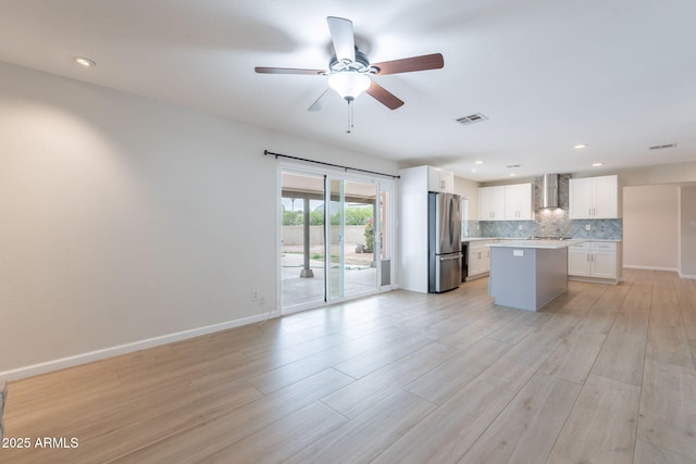 kitchen featuring freestanding refrigerator, wall chimney range hood, white cabinetry, a kitchen island, and recessed lighting