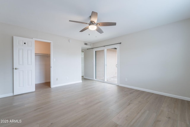unfurnished bedroom featuring baseboards, light wood-style flooring, a walk in closet, and ceiling fan