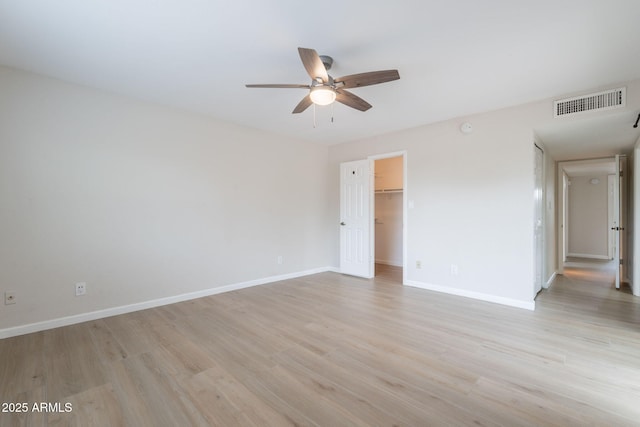 unfurnished bedroom featuring light wood-style flooring, baseboards, a spacious closet, and a closet
