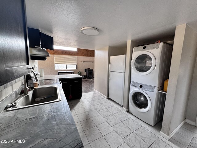 kitchen with stacked washer and dryer, light countertops, freestanding refrigerator, a sink, and under cabinet range hood