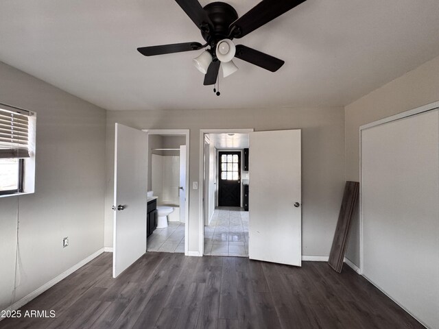 unfurnished bedroom with dark wood-style flooring, ensuite bath, a ceiling fan, and baseboards