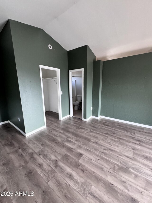 unfurnished bedroom featuring vaulted ceiling, a spacious closet, baseboards, and light wood-style floors