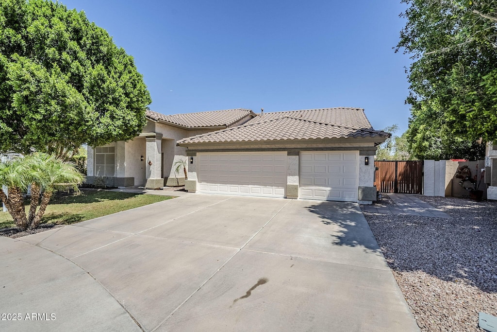 ranch-style home with a tile roof, concrete driveway, an attached garage, fence, and stucco siding