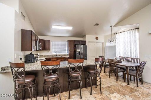 kitchen with dark brown cabinets, a kitchen breakfast bar, stainless steel appliances, sink, and light stone counters