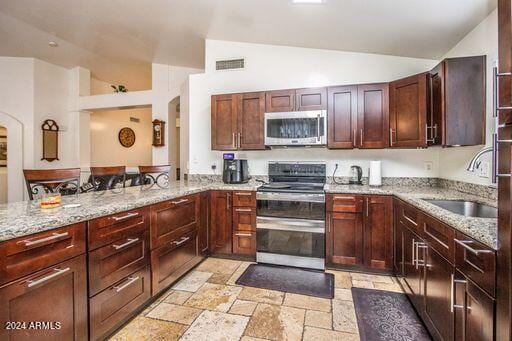 kitchen with lofted ceiling, sink, light stone counters, and stainless steel appliances