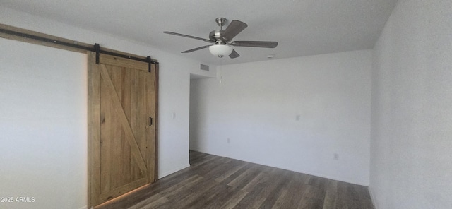 unfurnished bedroom featuring dark wood-type flooring, a ceiling fan, visible vents, and a barn door