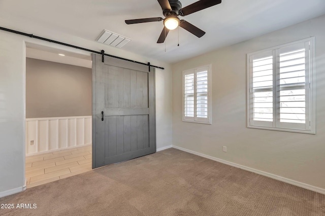 unfurnished bedroom with a barn door, ceiling fan, and carpet flooring