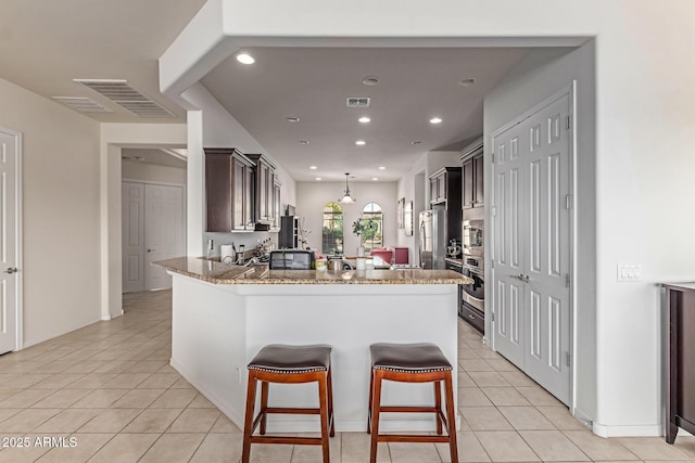 27105 W Marco Polo Rd, Buckeye, AZ 85396 - kitchen featuring stainless steel appliances, light tile patterned flooring, a peninsula, stone counters, and recessed lighting