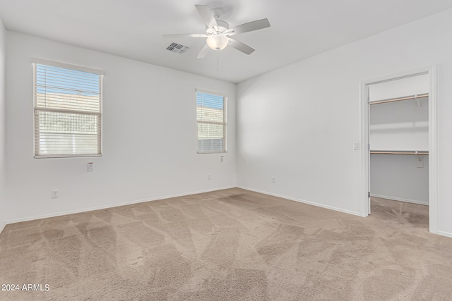 unfurnished bedroom featuring a closet, ceiling fan, light carpet, and a walk in closet