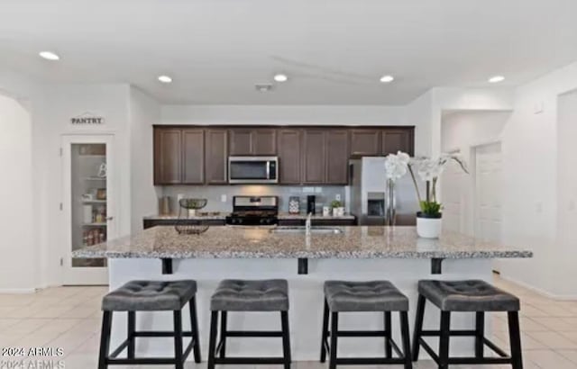 kitchen featuring a breakfast bar, stainless steel appliances, light stone counters, and an island with sink