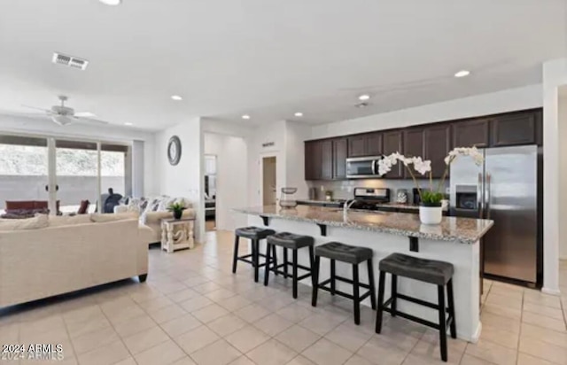 kitchen featuring appliances with stainless steel finishes, a breakfast bar, a kitchen island with sink, and dark brown cabinets