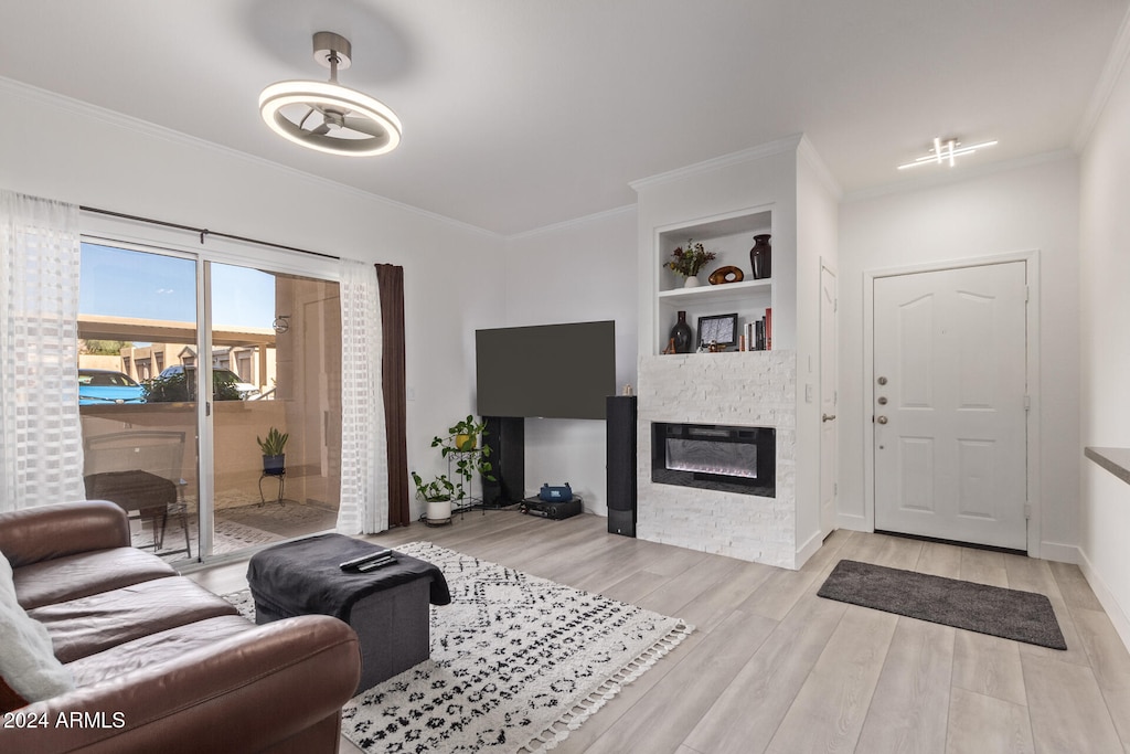 living room with light hardwood / wood-style floors, a stone fireplace, ornamental molding, and built in shelves