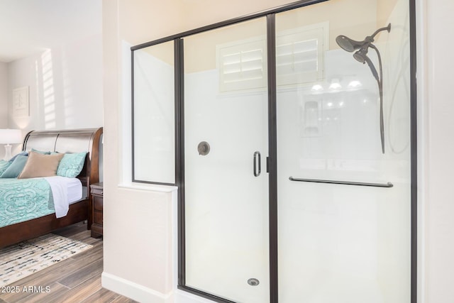 ensuite bathroom featuring wood finished floors, a stall shower, and baseboards
