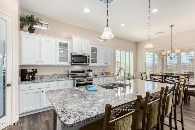 kitchen with stainless steel appliances, a sink, dark wood finished floors, a breakfast bar area, and a kitchen island with sink