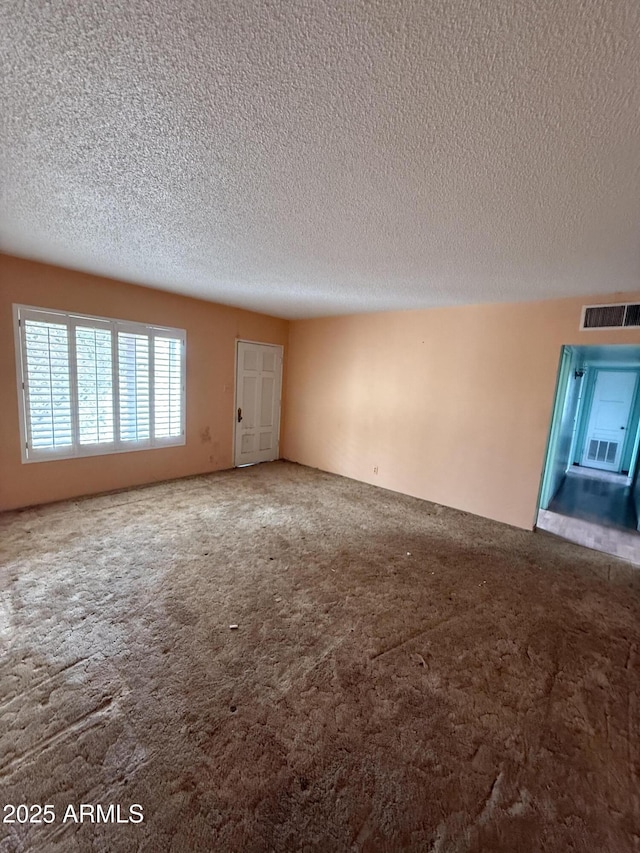 unfurnished room featuring a textured ceiling, carpet, and visible vents