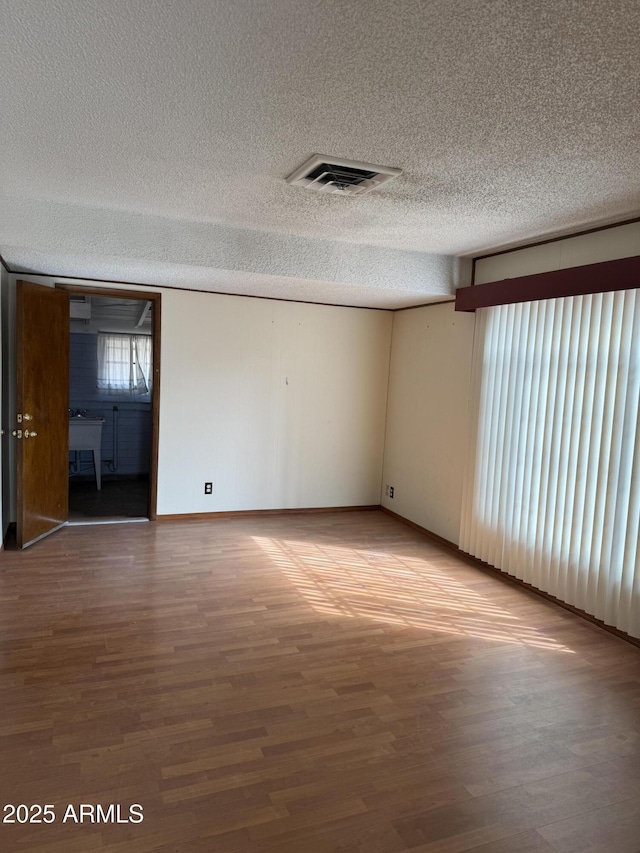 spare room featuring baseboards, visible vents, light wood-style flooring, and a textured ceiling