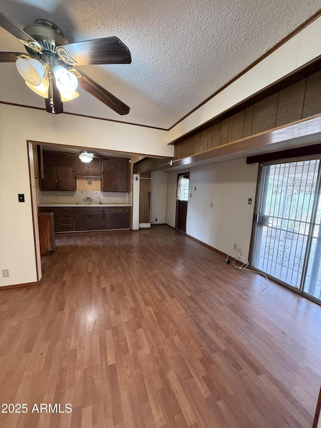 unfurnished living room with a textured ceiling, a ceiling fan, crown molding, and wood finished floors