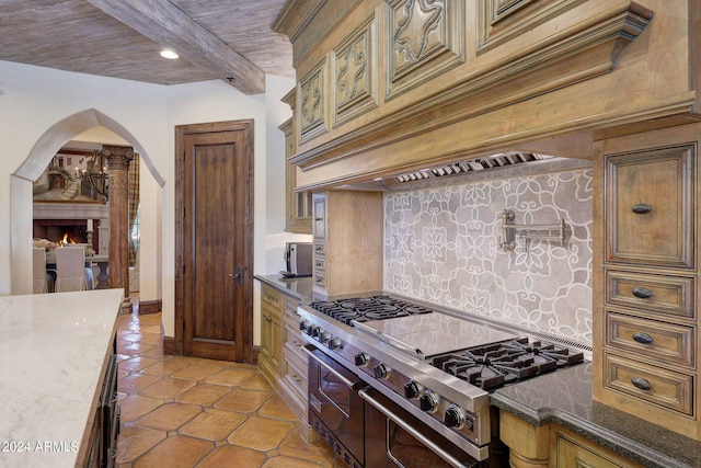 kitchen featuring high end stove, decorative backsplash, beamed ceiling, dark stone countertops, and light tile patterned flooring