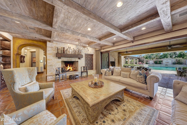 living room featuring ceiling fan with notable chandelier, wood ceiling, an outdoor stone fireplace, coffered ceiling, and beam ceiling