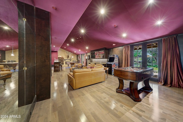 cinema room with french doors, light wood-type flooring, and vaulted ceiling