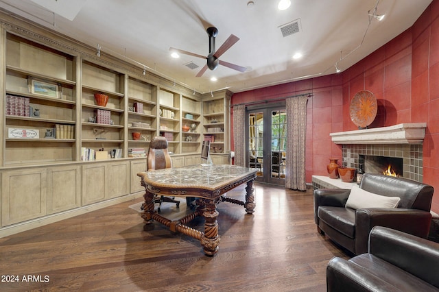 office area featuring built in shelves, dark hardwood / wood-style floors, a tile fireplace, and ceiling fan