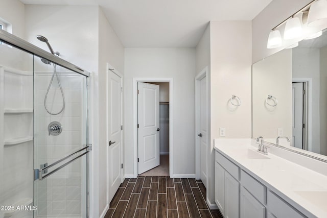 full bathroom with double vanity, wood tiled floor, a sink, a shower stall, and baseboards