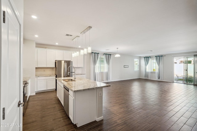 kitchen with a sink, white cabinets, open floor plan, a center island with sink, and decorative light fixtures