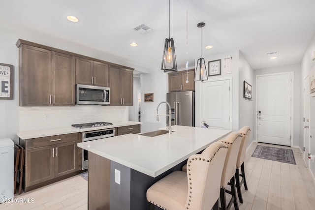 kitchen featuring sink, stainless steel appliances, decorative light fixtures, light hardwood / wood-style flooring, and a kitchen island with sink