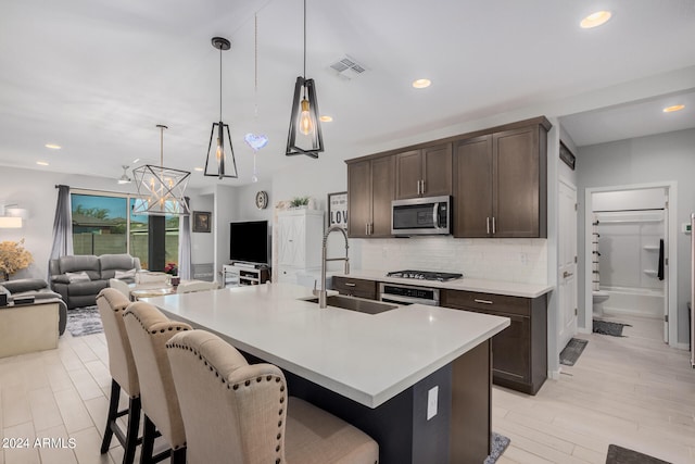 kitchen featuring a kitchen island with sink, a kitchen breakfast bar, stainless steel appliances, sink, and decorative light fixtures