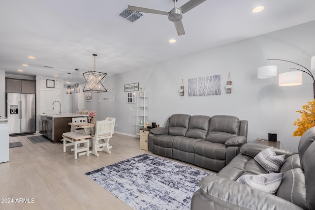 living room featuring light hardwood / wood-style flooring, sink, and ceiling fan with notable chandelier