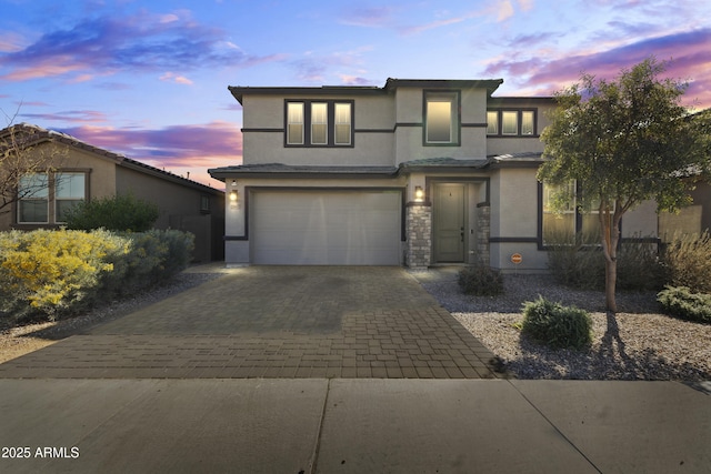 prairie-style house featuring decorative driveway, stone siding, an attached garage, and stucco siding