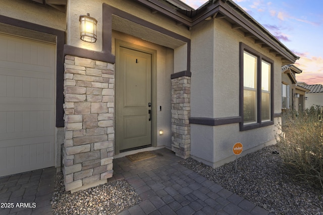 entrance to property with stone siding, stucco siding, and a garage