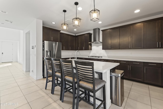 kitchen with light tile patterned floors, a breakfast bar, light countertops, appliances with stainless steel finishes, and wall chimney exhaust hood