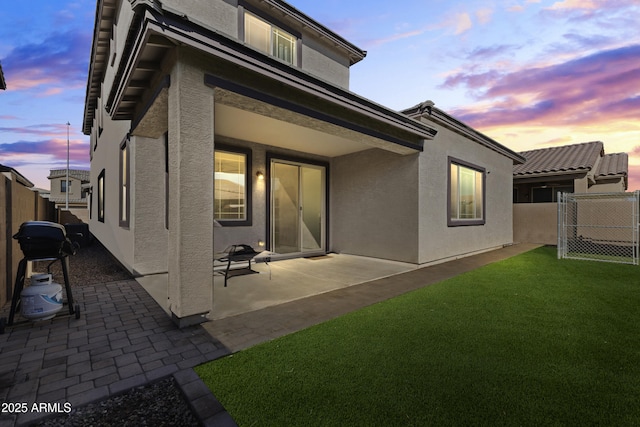 back of property at dusk featuring stucco siding, a patio, a yard, and a fenced backyard